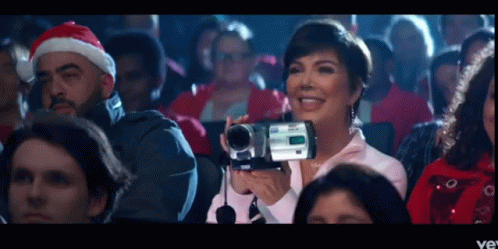 A Woman In A Santa Hat Is Holding A Video Camera GIF