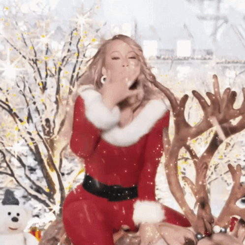 A Woman In A Santa Outfit Blowing A Kiss GIF