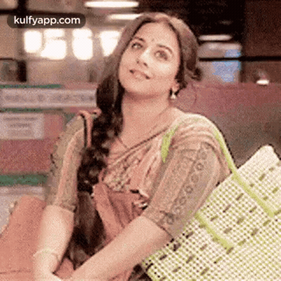 A Woman In A Saree Is Holding A Shopping Bag And Smiling While Sitting Down . GIF