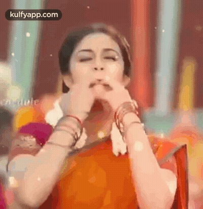 A Woman In A Saree Is Making A Funny Face With Her Hands . GIF