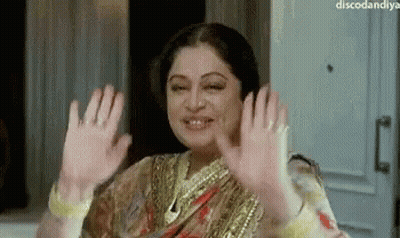 A Woman In A Sari Is Waving Her Hands In The Air And Smiling . GIF