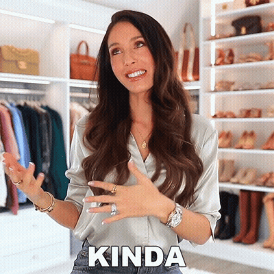 A Woman In A Satin Shirt Says Kinda In Front Of A Closet Full Of Shoes GIF