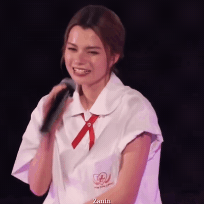 A Woman In A School Uniform Is Holding A Microphone And Smiling . GIF