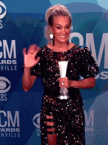 A Woman In A Sequined Dress Is Holding A Trophy In Front Of A Wall That Says Cm Awards GIF