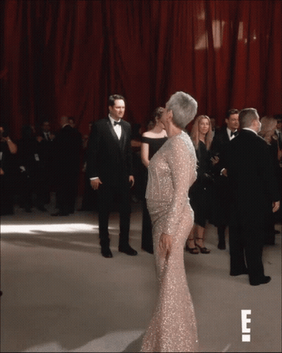 A Woman In A Sequined Dress Is Kissing A Man In A Tuxedo On A Red Carpet GIF