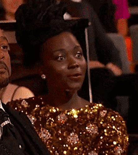 A Woman In A Sequined Dress Is Sitting In A Crowd Of People . GIF