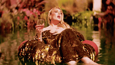 A Woman In A Sequined Dress Is Sitting On A Raft In The Water Holding A Glass Of Wine . GIF