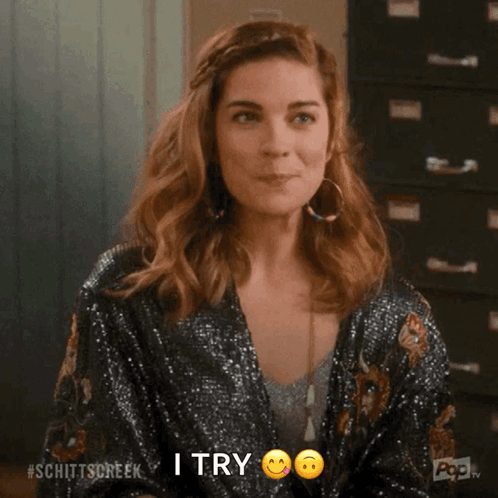 A Woman In A Sequined Jacket Is Smiling And Making A Peace Sign With Her Finger . GIF