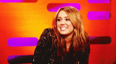 A Woman In A Sequined Jacket Smiles In Front Of A Purple And Orange Background GIF