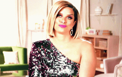A Woman In A Sequined One Shoulder Dress Is Sitting In A Living Room GIF