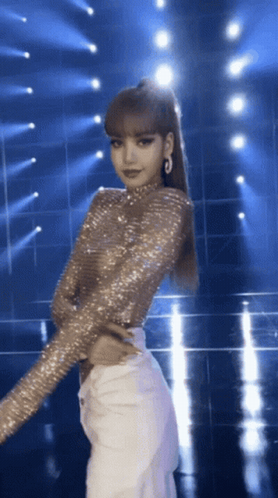 A Woman In A Sequined Top And White Pants Stands On A Stage GIF