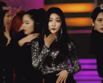 A Woman In A Sequined Top Stands In Front Of A Group Of Girls GIF