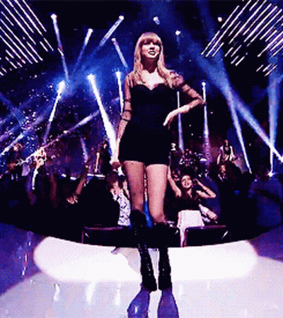 A Woman In A Short Black Dress Is Standing On A Stage In Front Of A Crowd GIF