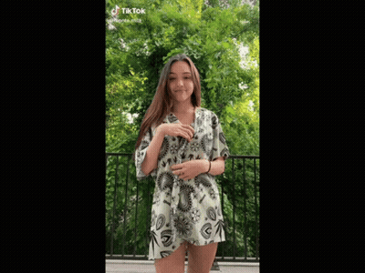 A Woman In A Short Dress Is Standing On A Balcony With Trees In The Background GIF