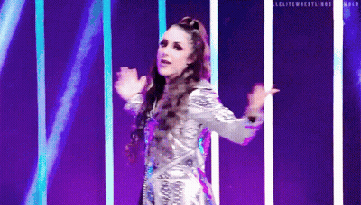 A Woman In A Silver Dress Is Dancing On A Stage In Front Of Purple Lights . GIF