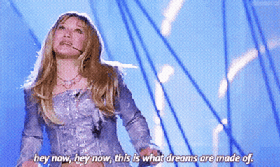 A Woman In A Silver Dress Is Standing On A Stage And Saying Hey Now Hey Now This Is What Dreams Are Made Of GIF