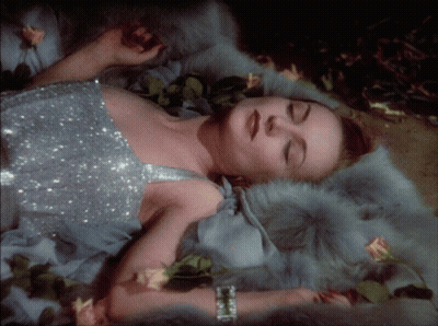 A Woman In A Silver Dress Laying On A Fur Blanket GIF