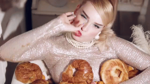 A Woman In A Silver Sequined Dress Is Holding A Tray Of Bread GIF
