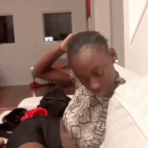 A Woman In A Snake Print Shirt Is Sitting On A Couch Holding Her Head . GIF