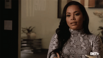 A Woman In A Snake Print Turtleneck Sweater Is Standing In Front Of A Bet Sign GIF