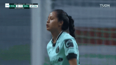 A Woman In A Soccer Uniform Stands In Front Of A Tv Screen That Says Tudn On It GIF