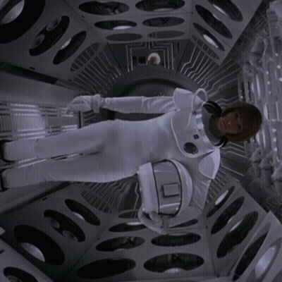 A Woman In A Space Suit Is Holding A Helmet With The Letter O On It GIF