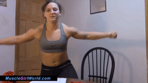 A Woman In A Sports Bra Is Standing In Front Of A Chair With The Website Musclegirlworld.com Written On The Bottom GIF