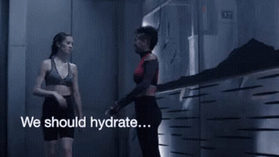 A Woman In A Sports Bra Is Walking Down A Hallway With The Words We Should Hydrate GIF