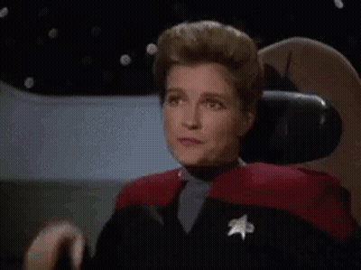 A Woman In A Star Trek Uniform Is Sitting In A Chair And Making A Face . GIF