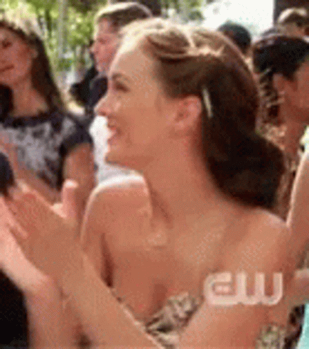 A Woman In A Strapless Dress Is Clapping In A Crowd Of People . GIF