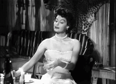 A Woman In A Strapless Dress Is Sitting At A Table With A Candle . GIF