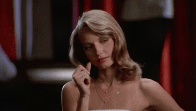 A Woman In A Strapless Dress Is Sitting At A Table With Her Hand In Her Hair . GIF