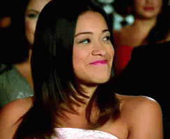 A Woman In A Strapless Dress Is Smiling In Front Of A Group Of Women . GIF