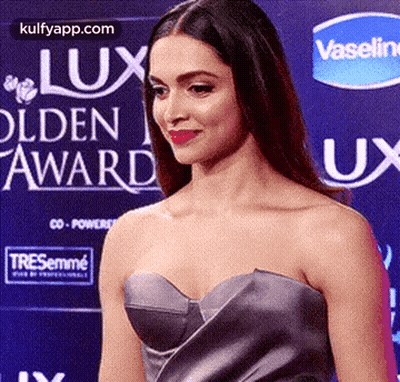 A Woman In A Strapless Dress Is Standing On A Red Carpet In Front Of A Vaseline Sign . GIF