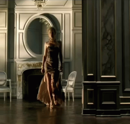 A Woman In A Strapless Dress Walks Through A Room GIF