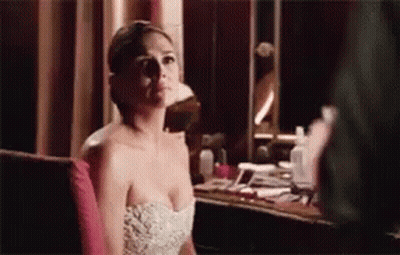 A Woman In A Strapless White Dress Is Sitting In Front Of A Mirror . GIF