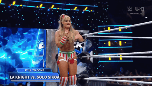 A Woman In A Striped Outfit Is Standing In A Wrestling Ring With A Sign That Says Still To Come GIF
