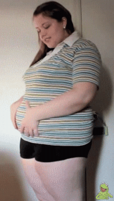 A Woman In A Striped Shirt And Black Shorts Holds Her Stomach GIF