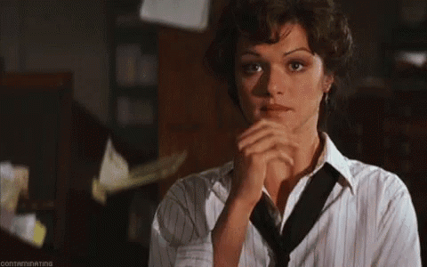 A Woman In A Striped Shirt And Tie Is Looking At The Camera With Her Hands Folded . GIF