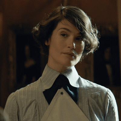 A Woman In A Striped Shirt And Tie Looks At The Camera GIF