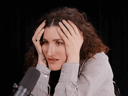 A Woman In A Striped Shirt Holds Her Head In Her Hands GIF