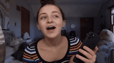 A Woman In A Striped Shirt Is Holding A Cell Phone GIF