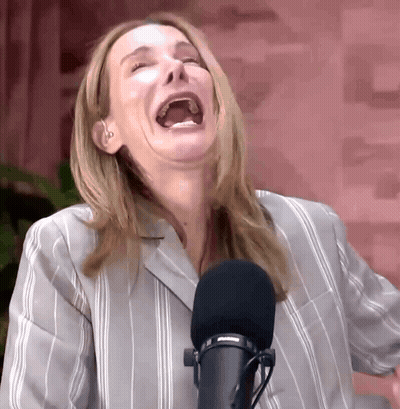 A Woman In A Striped Shirt Is Laughing In Front Of A Microphone GIF