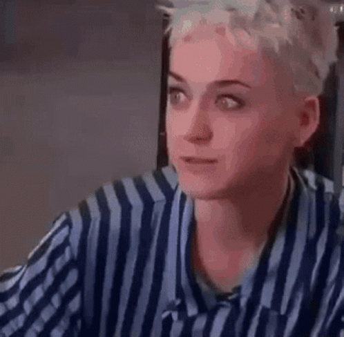 A Woman In A Striped Shirt Is Sitting At A Table Drinking A Glass Of Wine . GIF