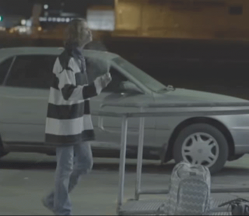 A Woman In A Striped Shirt Is Standing In Front Of A Car GIF