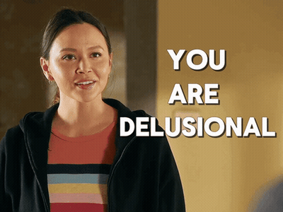 A Woman In A Striped Shirt Is Standing In Front Of A Sign That Says " You Are Delusional " GIF