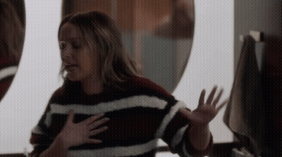 A Woman In A Striped Sweater Is Looking At Herself In A Mirror GIF