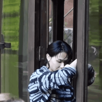 A Woman In A Striped Sweater Is Standing In Front Of A Glass Door . GIF