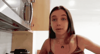 A Woman In A Striped Tank Top Is Standing In A Kitchen Next To A Microwave GIF
