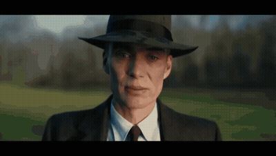A Woman In A Suit And Hat Is Looking At The Camera . GIF